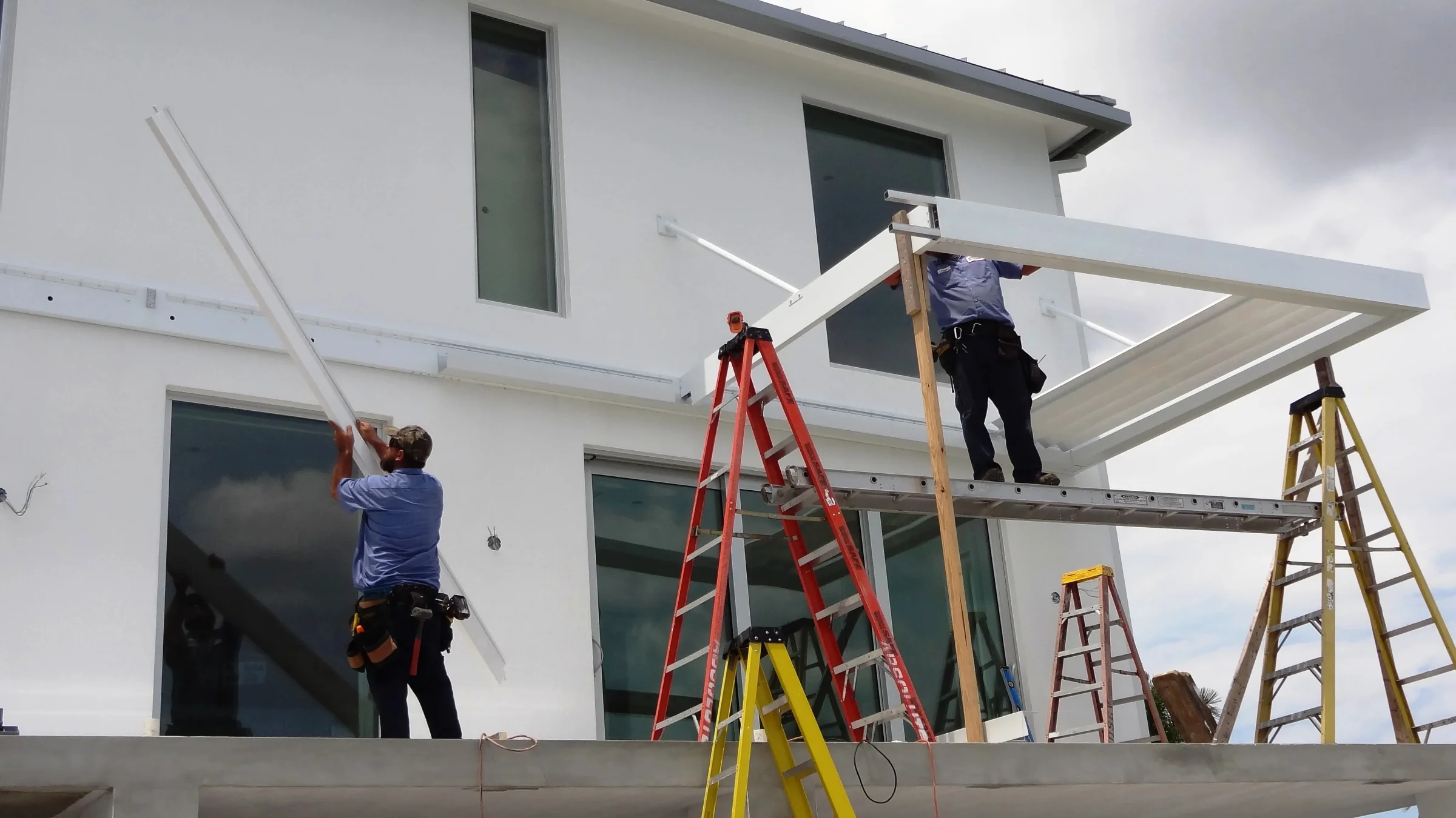 StruXure installation technicians on ladders mounting a white aluminum pergola frame to a Florida home