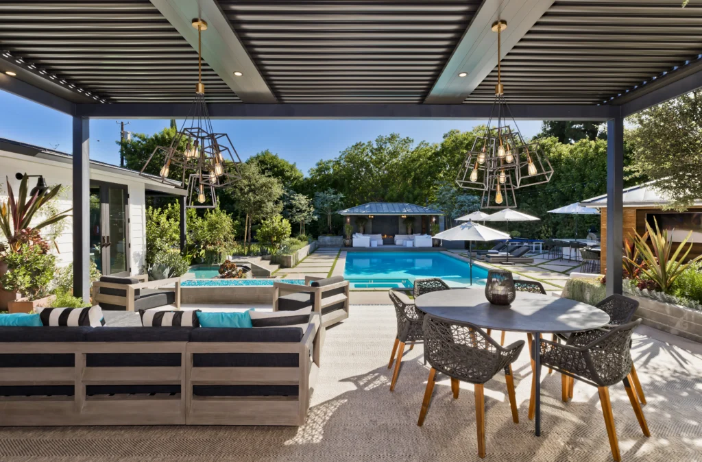 Louvered pergola over a lounge and dining area beside a pool with umbrellas beyond