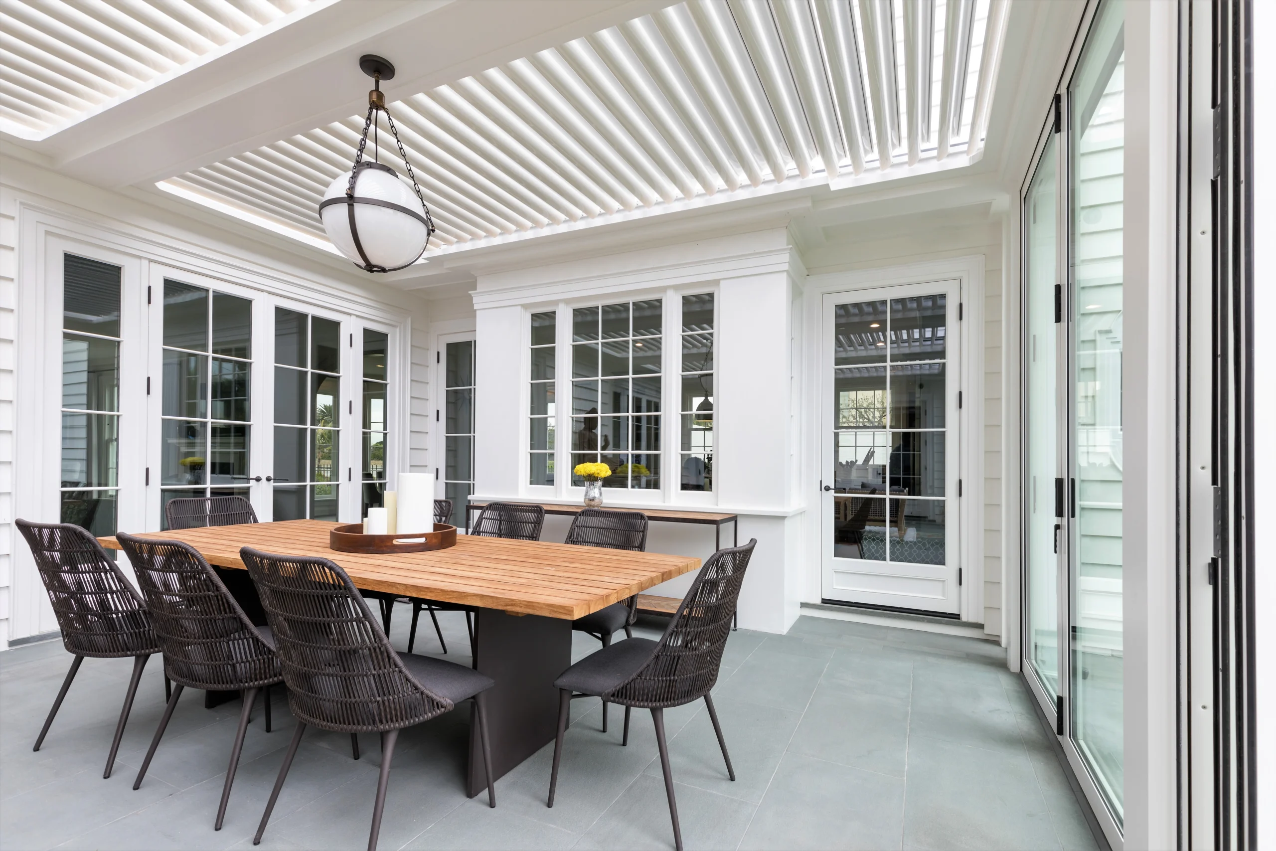 Interior view of a covered outdoor room with white louvered ceiling and folding glass doors