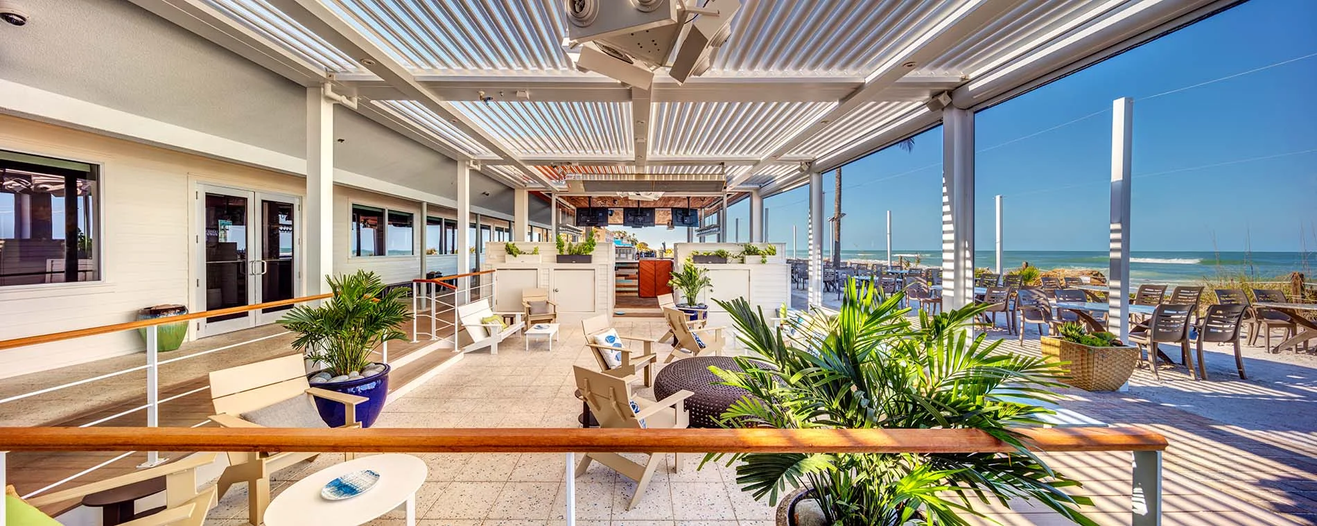 Covered waterfront restaurant terrace with a louvered roof, palms and boats in the background