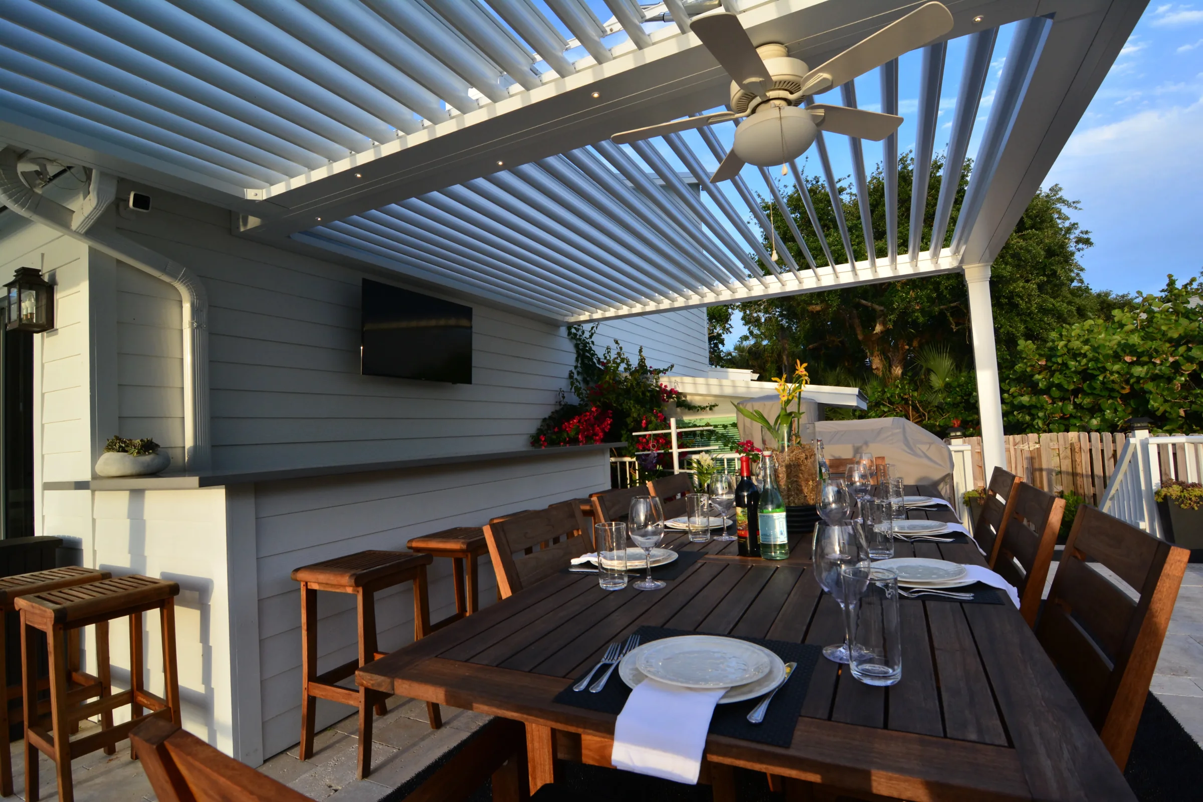 Covered outdoor bar and dining area under an open aluminum louvered roof with tropical planting
