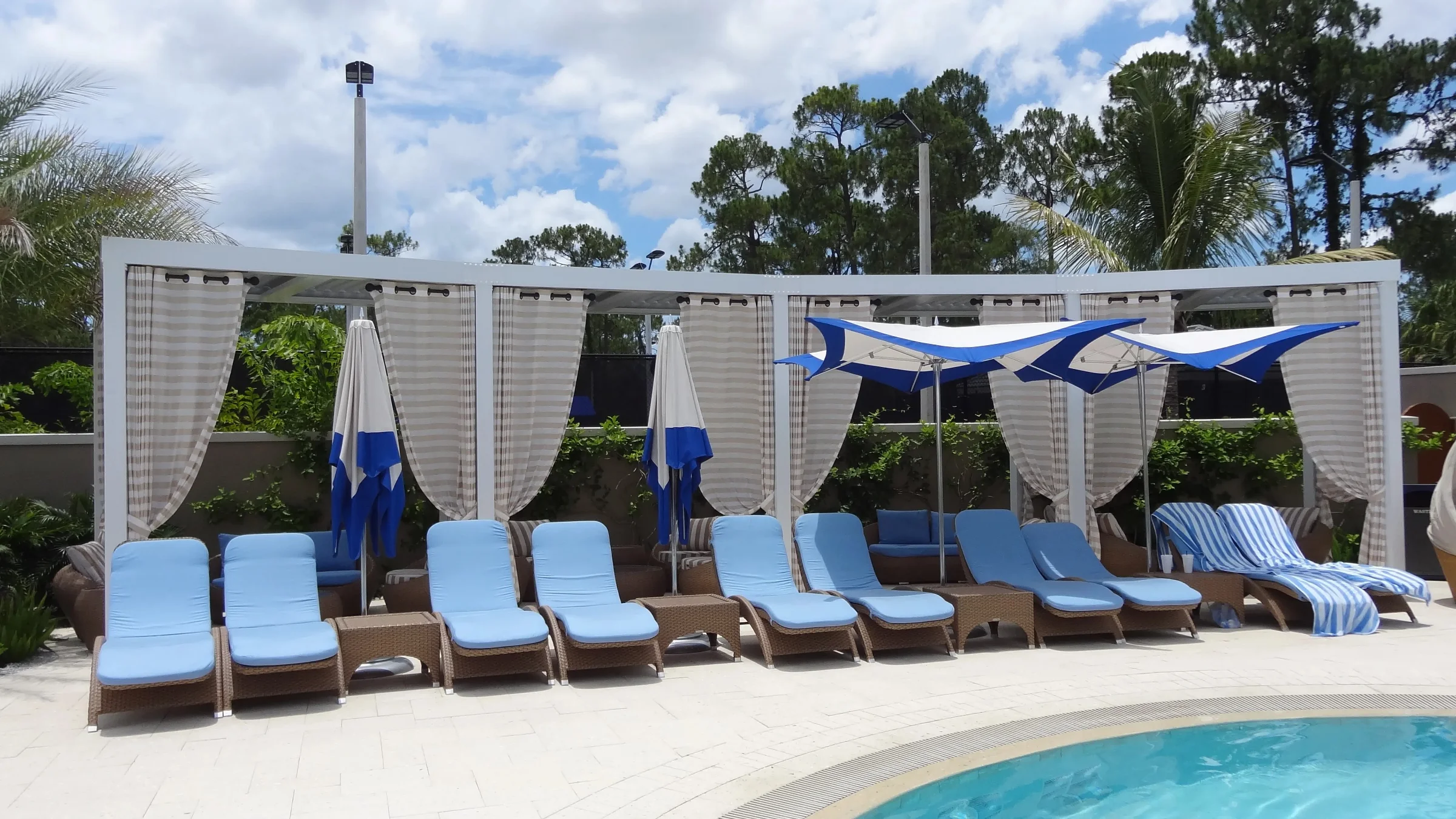 Grey Oaks pool deck with blue loungers, sail shades, and a white StruXure pergola structure