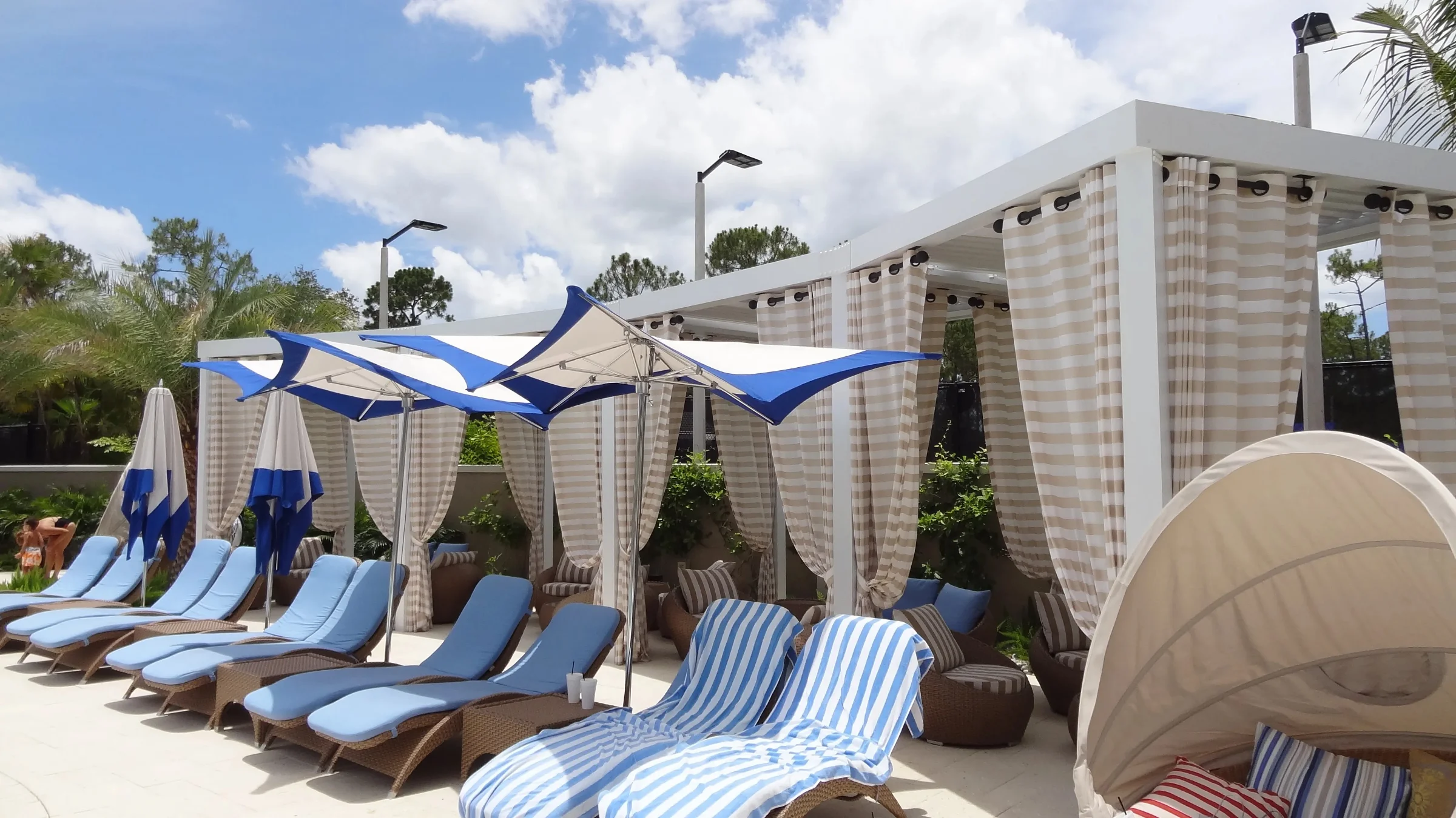 Wide view of the Grey Oaks pool area with blue lounge chairs, sail shades, and StruXure cabana structures