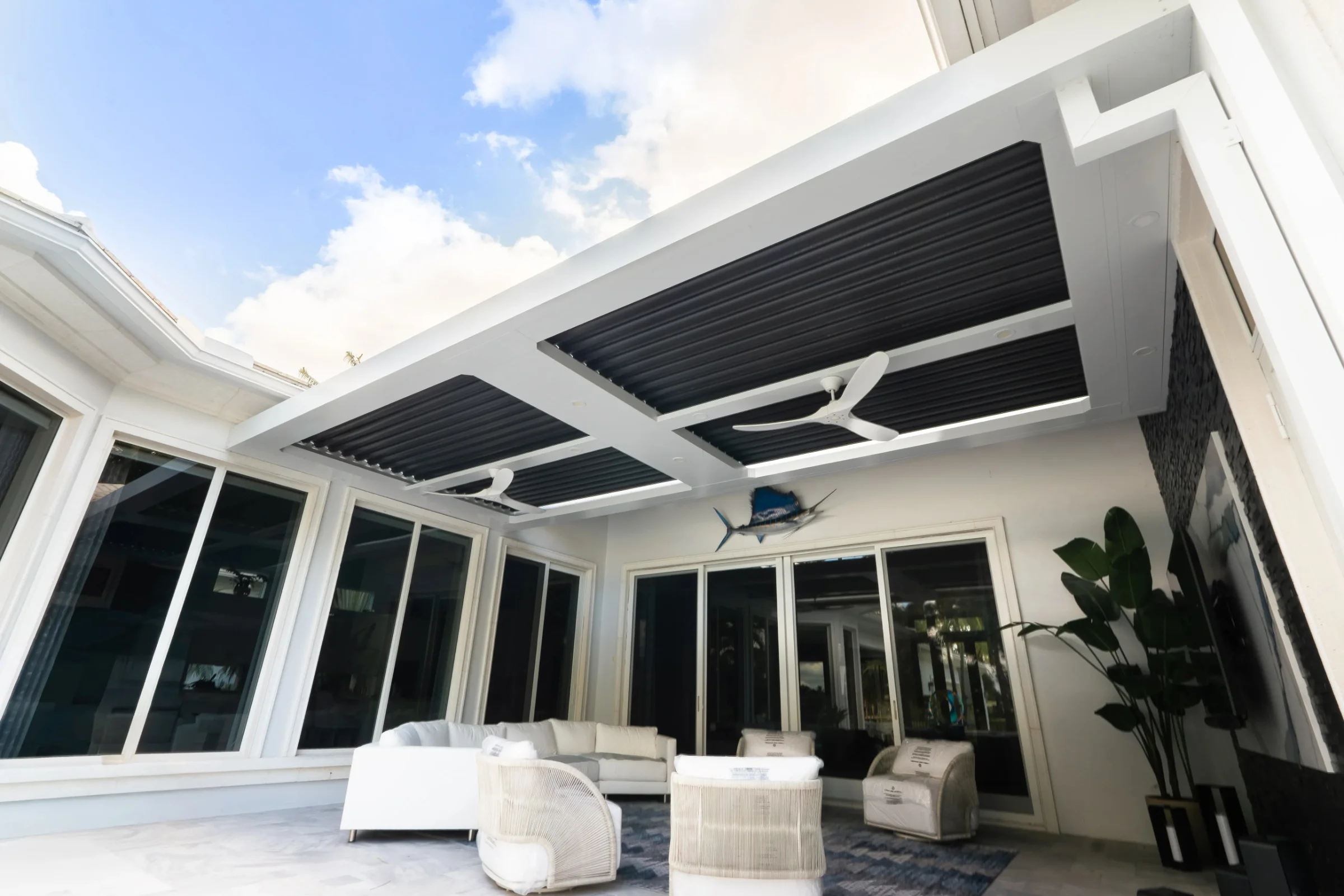 Underside of an aluminum louvered roof with glass walls under a blue Florida sky