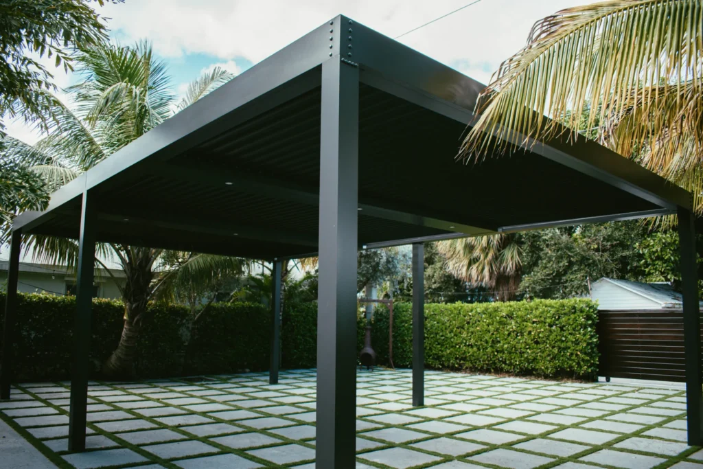 Dark charcoal StruXure louvered pergola with closed louvers over a stone patio framed by tropical palms