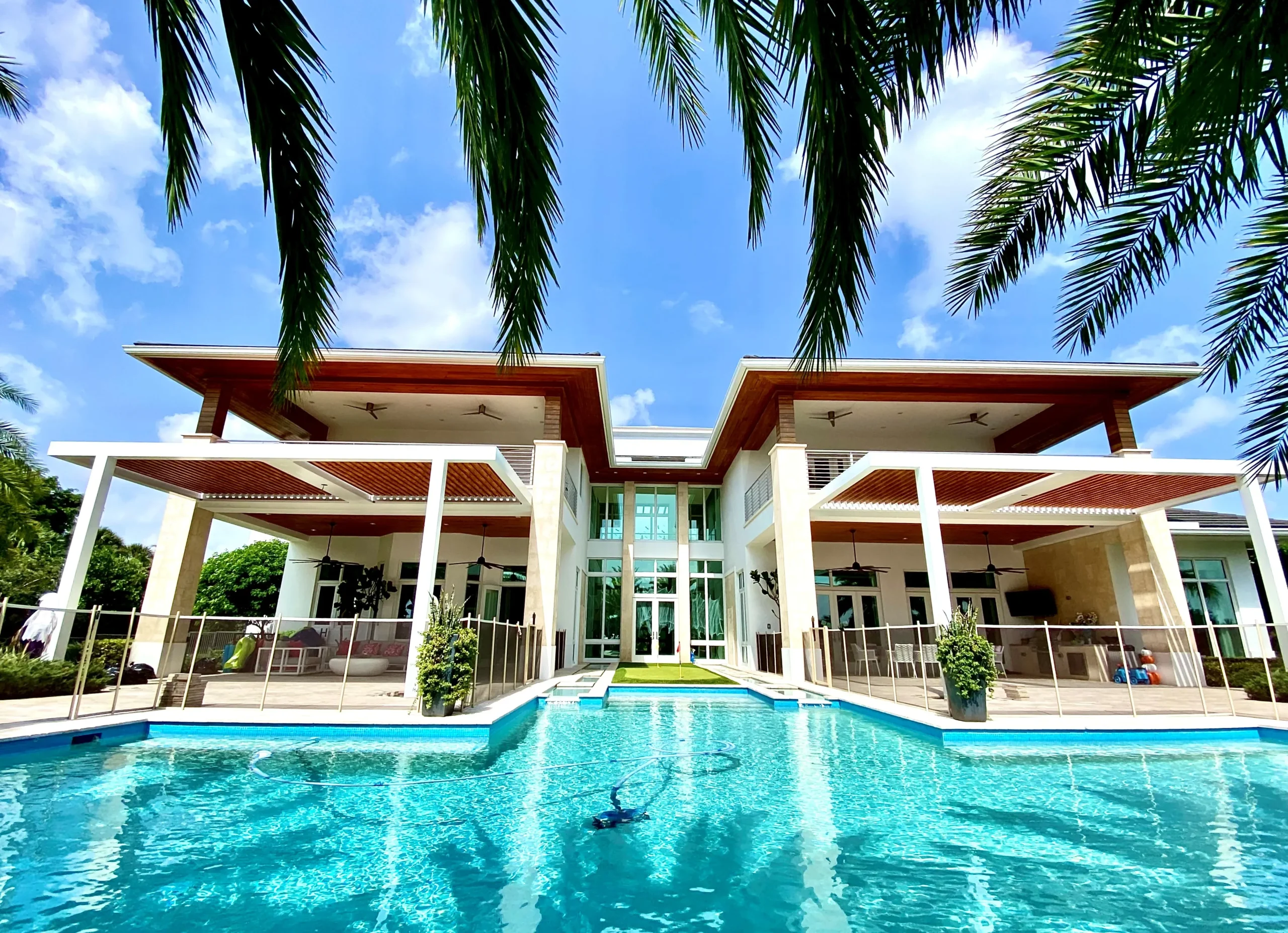Aluminum pergola with wood-grain louvers over a South Florida pool surrounded by palms