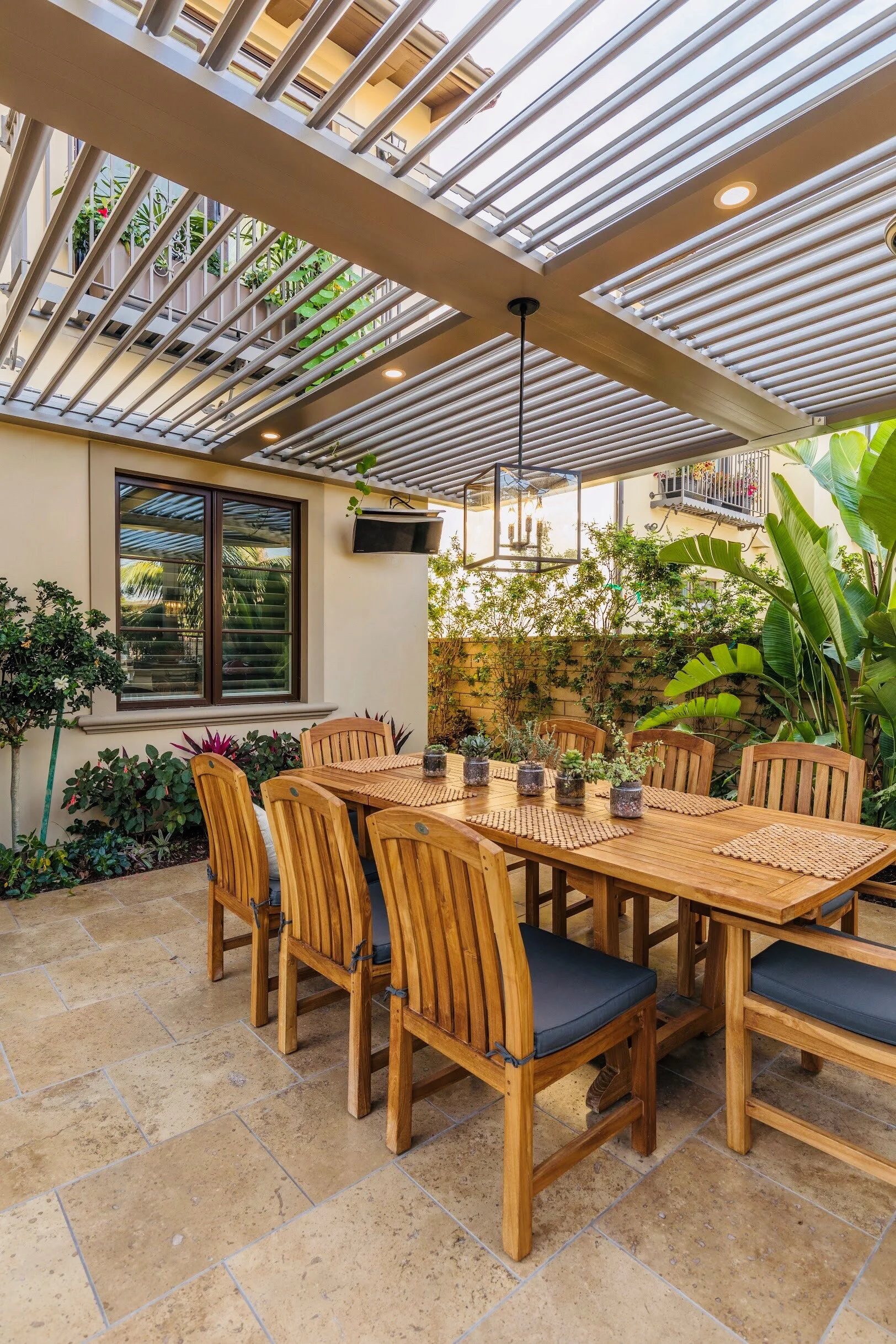 Dining area beneath a louvered pergola with a fan beam and tropical planting in South Florida
