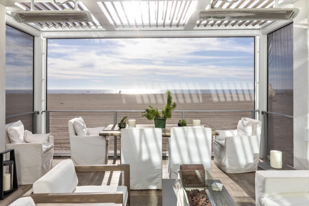 White StruXure pergola with motorized drop screens partially deployed on a South Florida beachfront deck