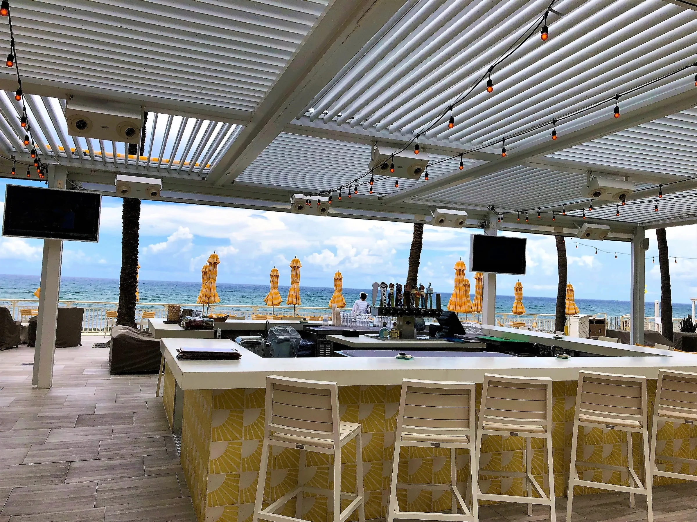 Guests seated at an outdoor bar beneath an operable louvered roof with ocean views in South Florida