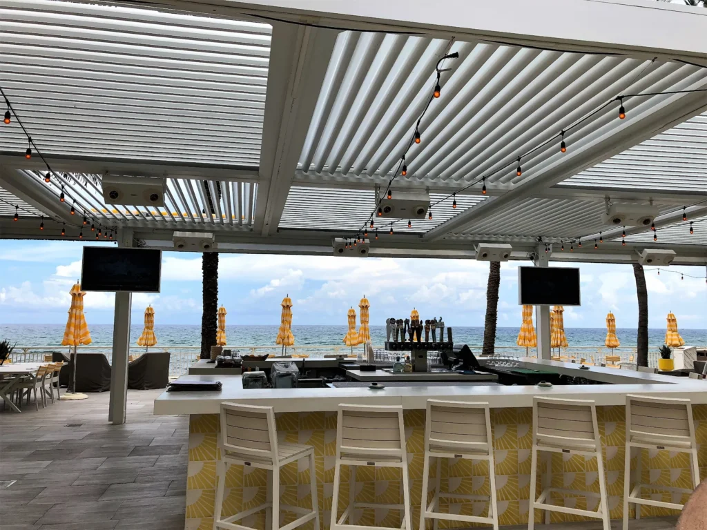 White StruXure louvered pergola with string lights over a beachfront resort bar at dusk in South Florida