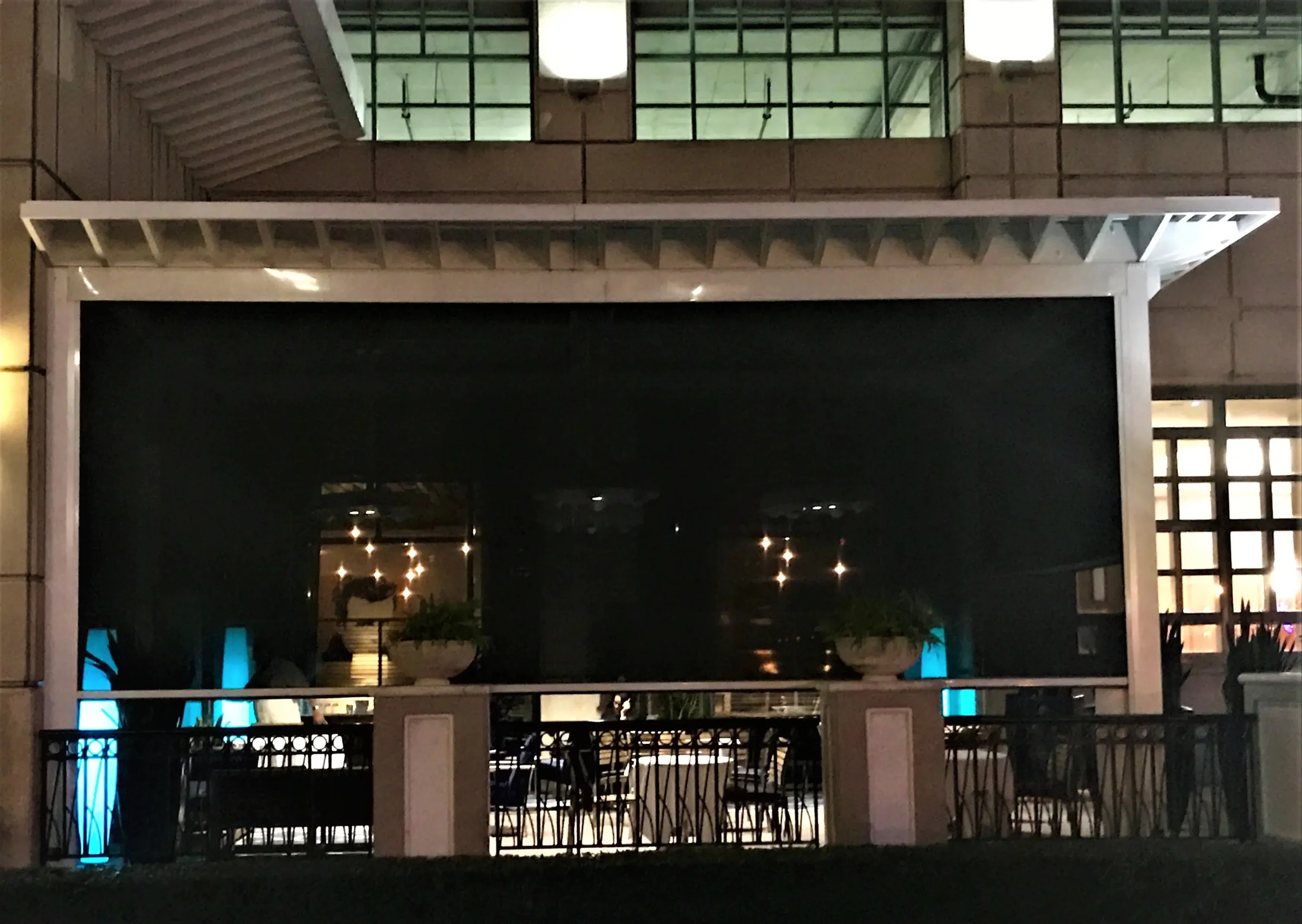 Screens lowered at dusk on a retrofitted restaurant terrace with the interior lit behind the mesh