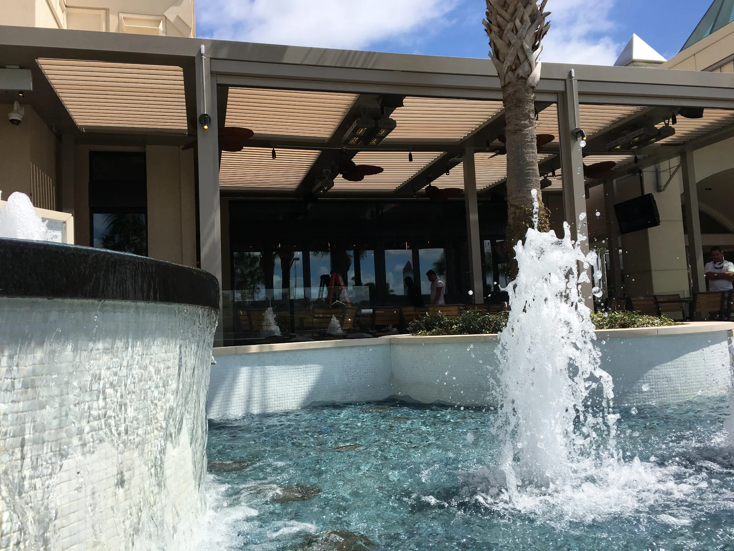 Tiki hut vs pergola: a louvered aluminum pergola shading a Palm Beach Gardens patio beside a fountain