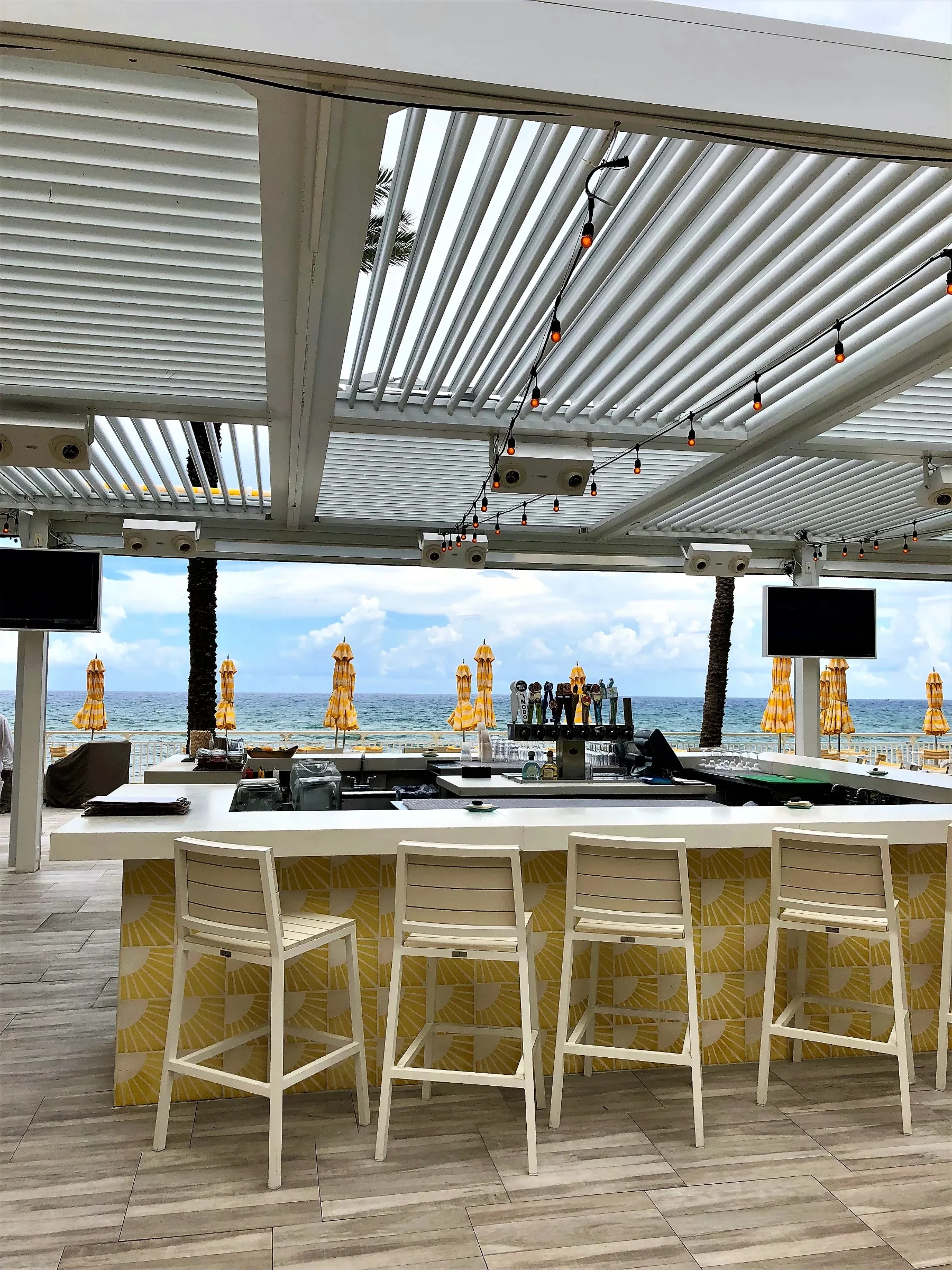 White aluminum StruXure louvered pergola canopy over outdoor bar and dining area at EAU Palm Beach Resort