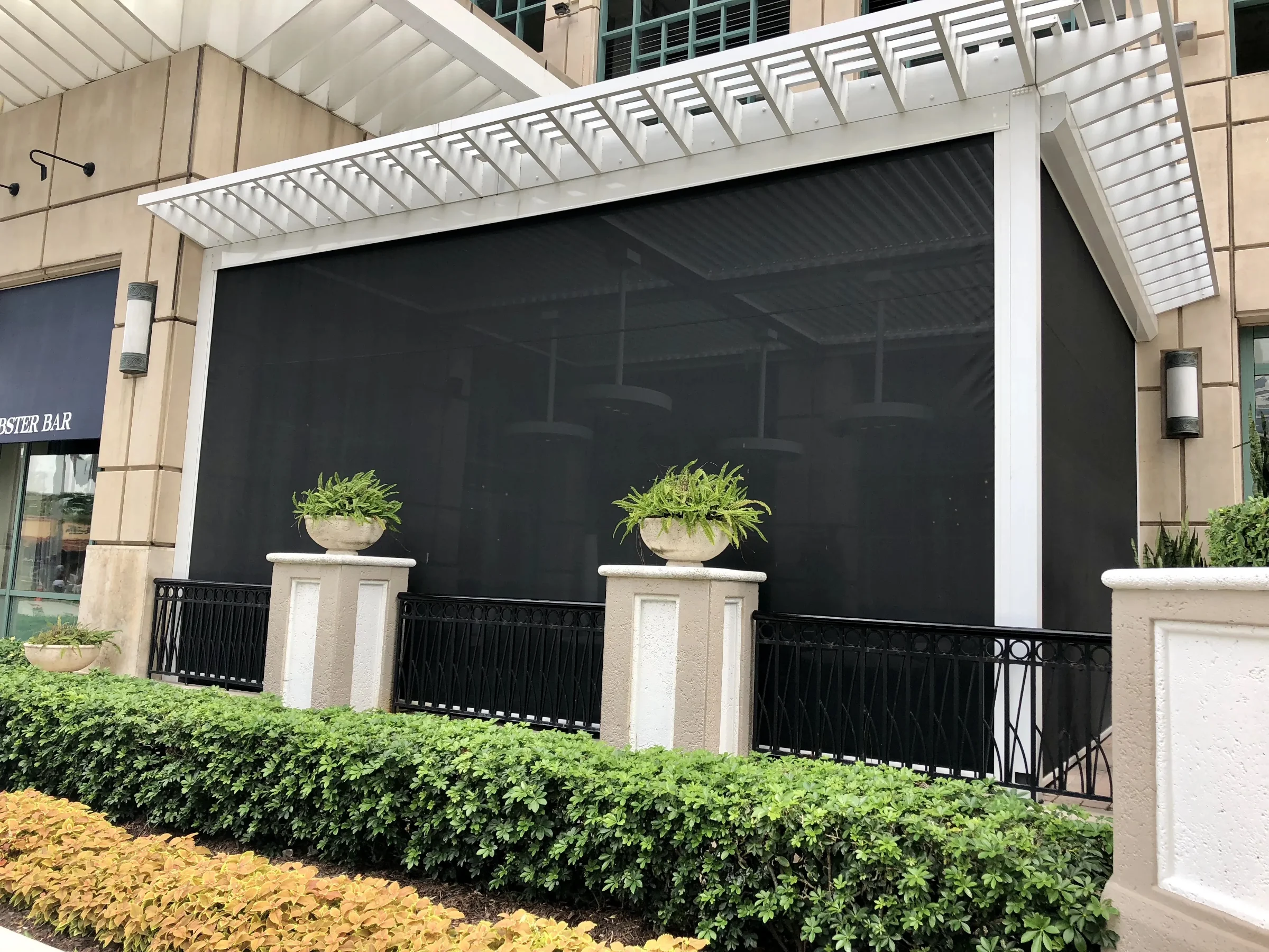 Retrofit motorized screens fully lowered in side tracks across a covered terrace opening