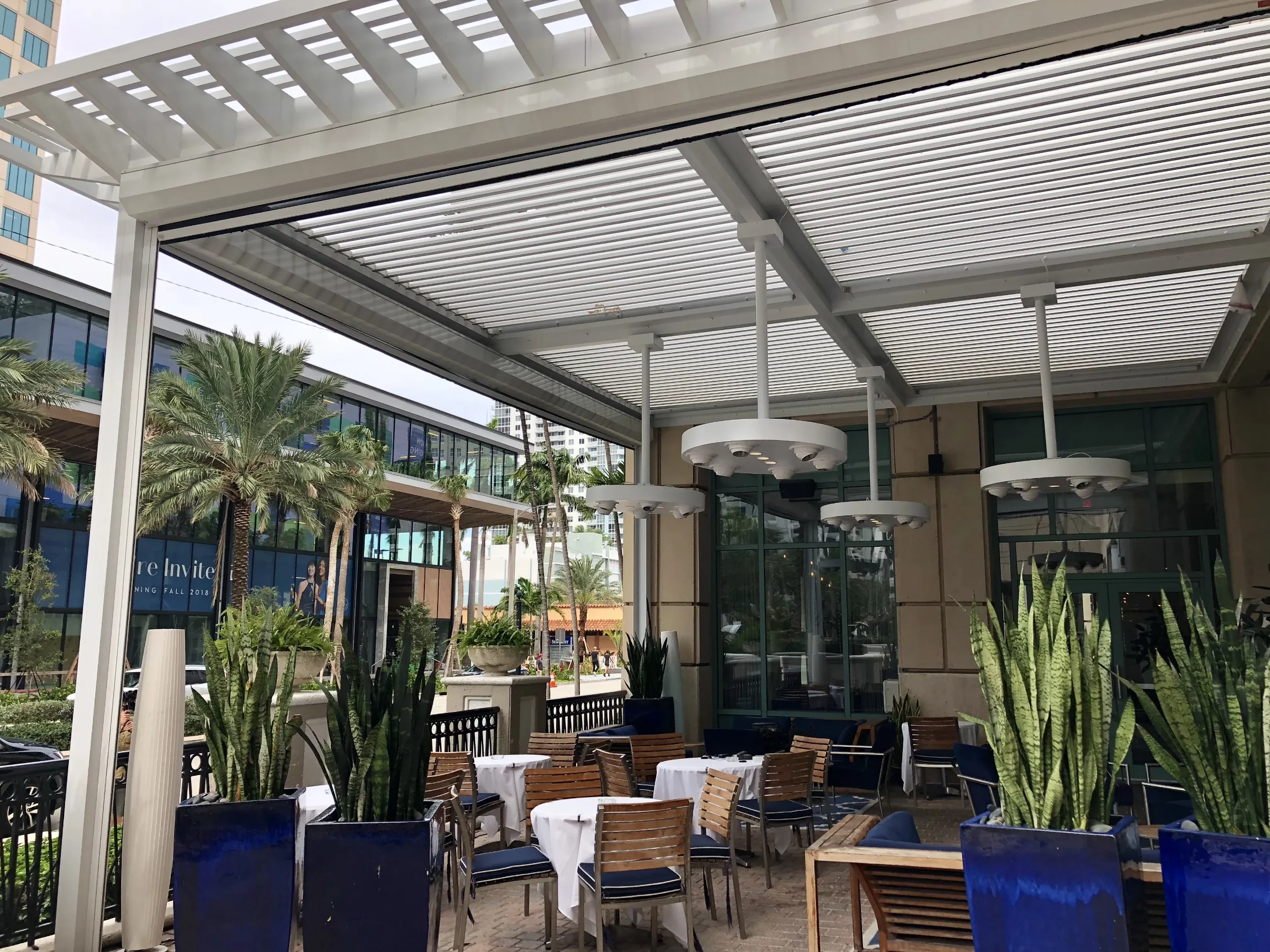 Louvered pergola with motorised screen tracks on a Fort Lauderdale restaurant patio, screens retracted