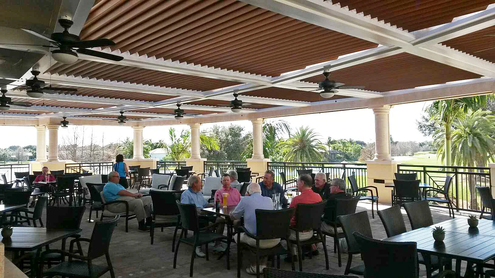 Diners seated beneath a louvered pergola on a terrace overlooking a golf course in South Florida