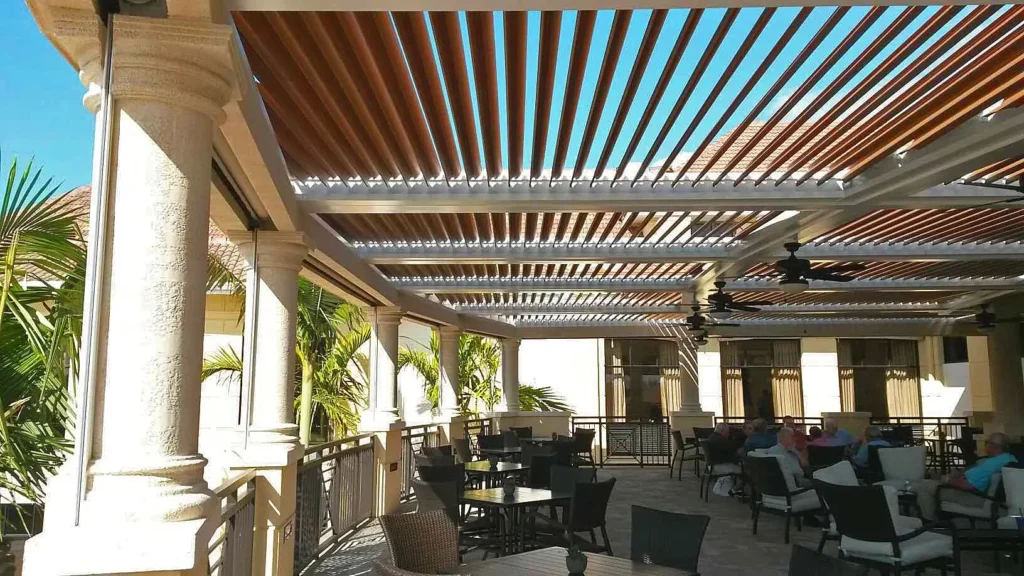 Wood-grain louvered roof over a shaded terrace with ceiling fans, an equestrian pergola style that suits a barn courtyard