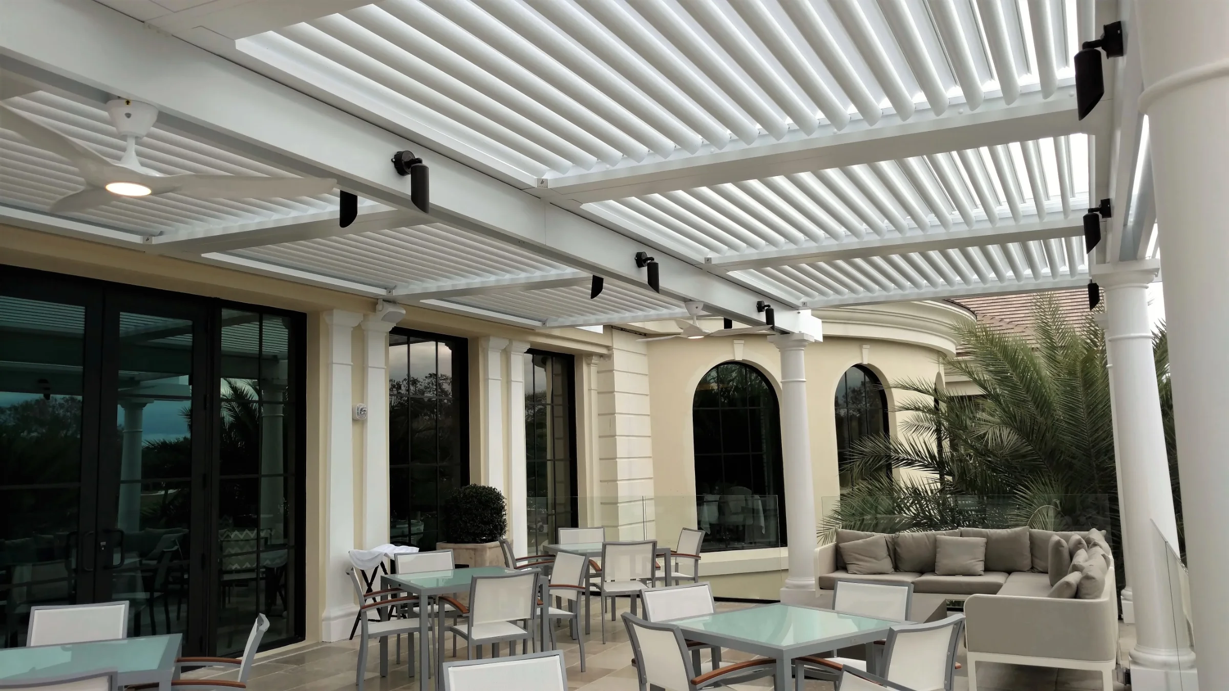 Outdoor dining and lounge amenity area under white StruXure louvered pergolas at a country club