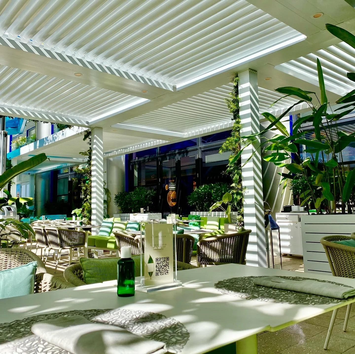 Louvered pergola roof closed over a planted Miami courtyard during a rain shower