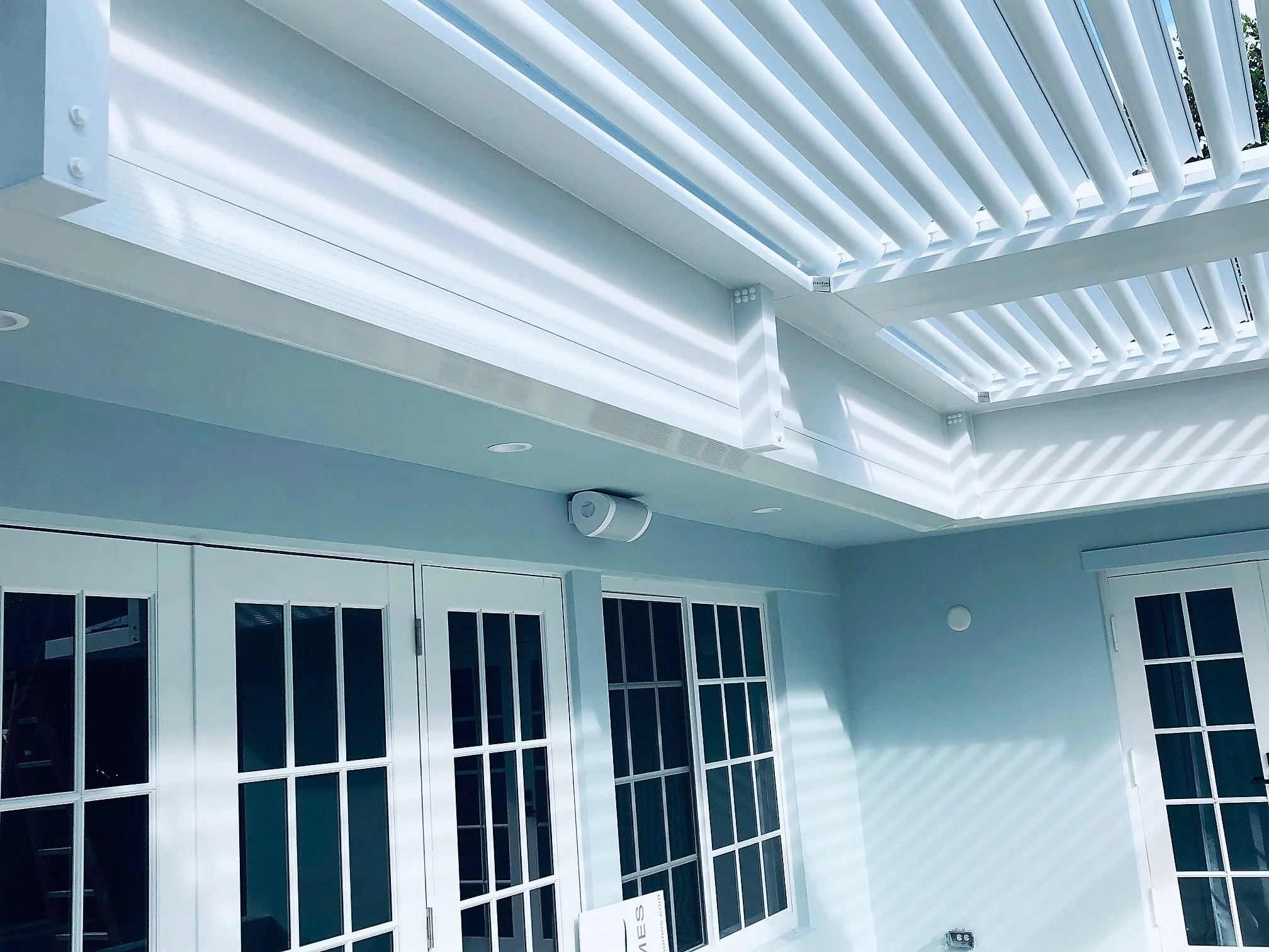 Underside of a louvered roof carried on a pergola riser wall above french doors