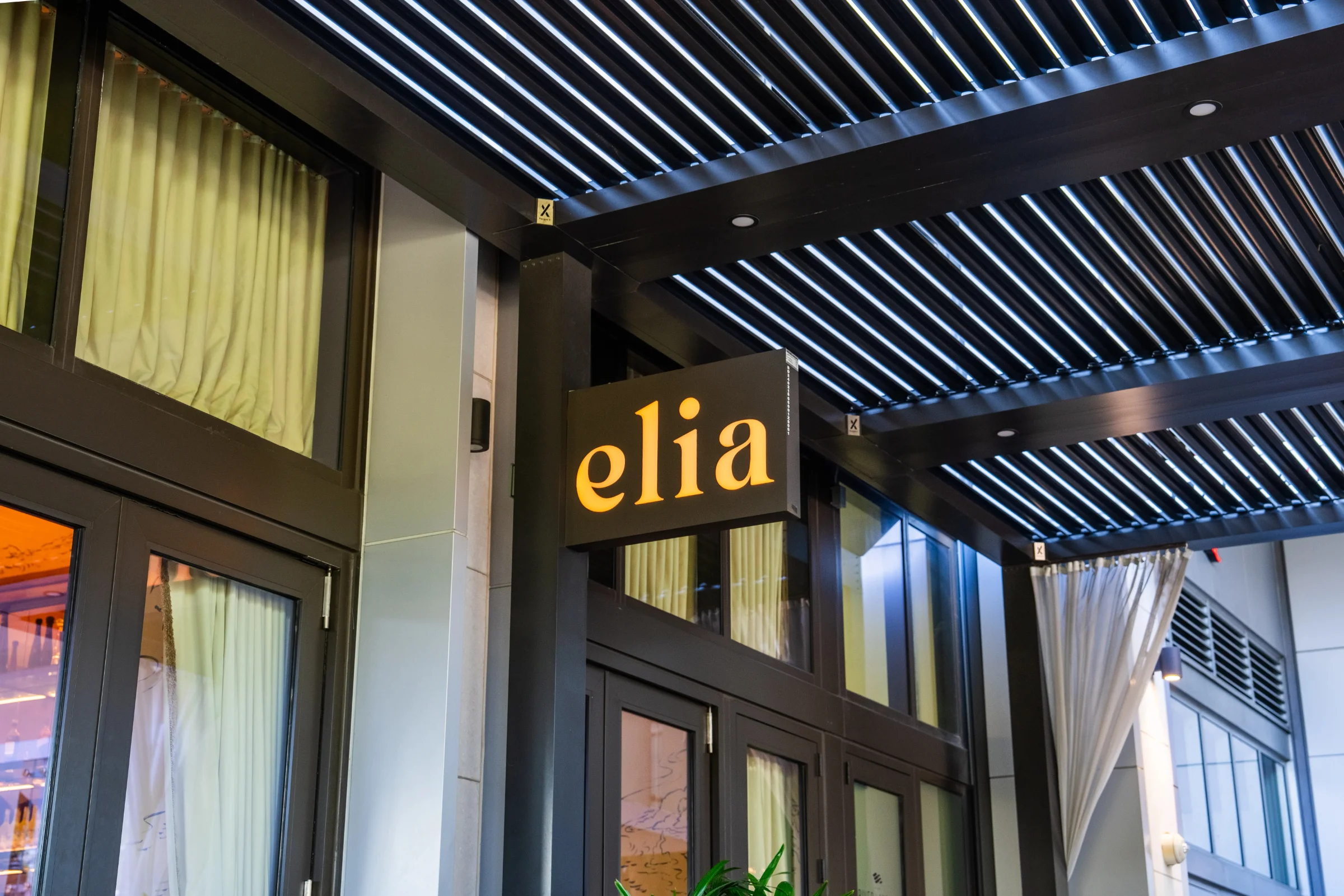 Louvered shade structure over a retail walkway entrance with storefront signage