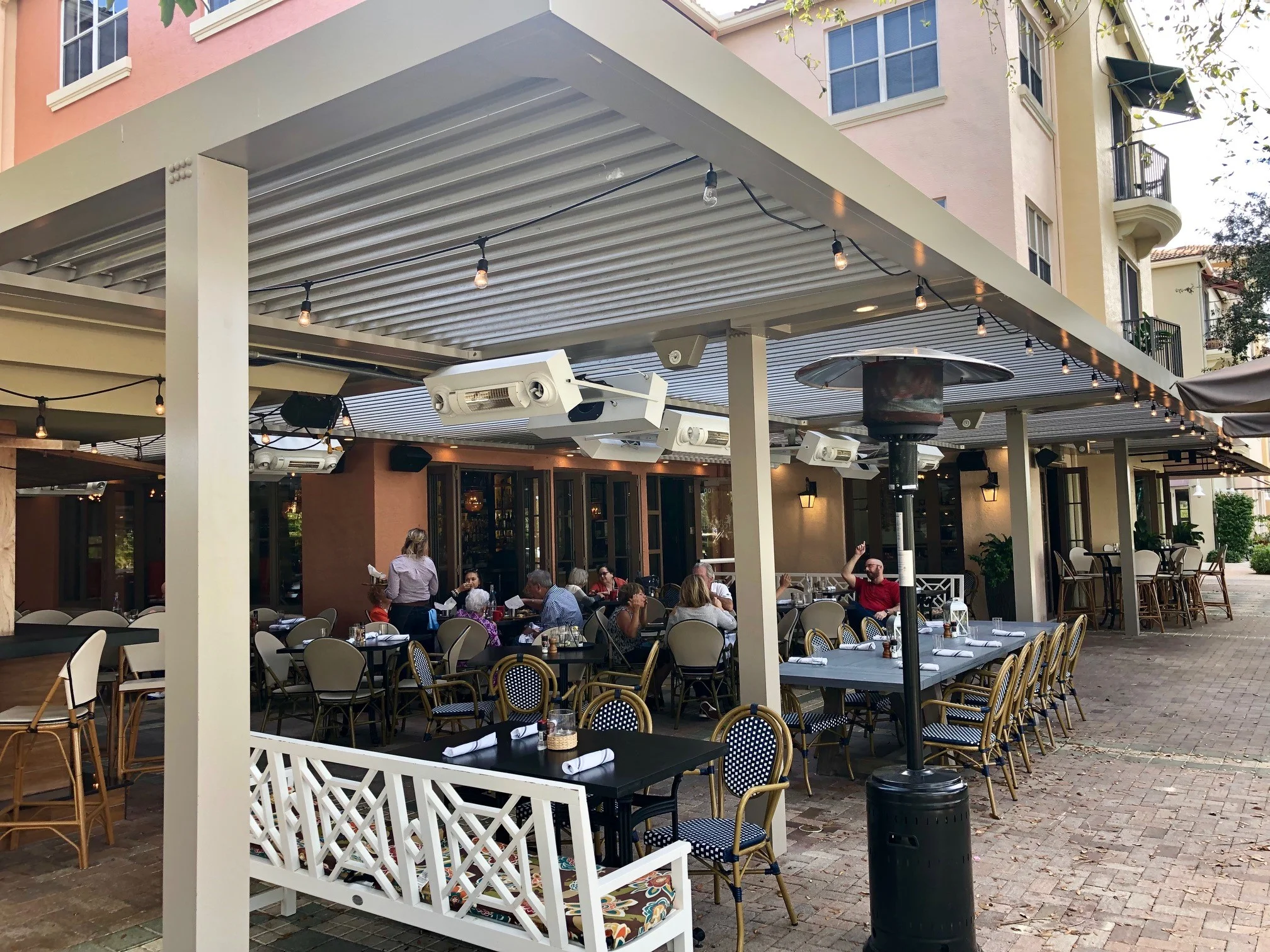 Covered patio under a louvered roof with overhead heaters and lighting mounted between the beams