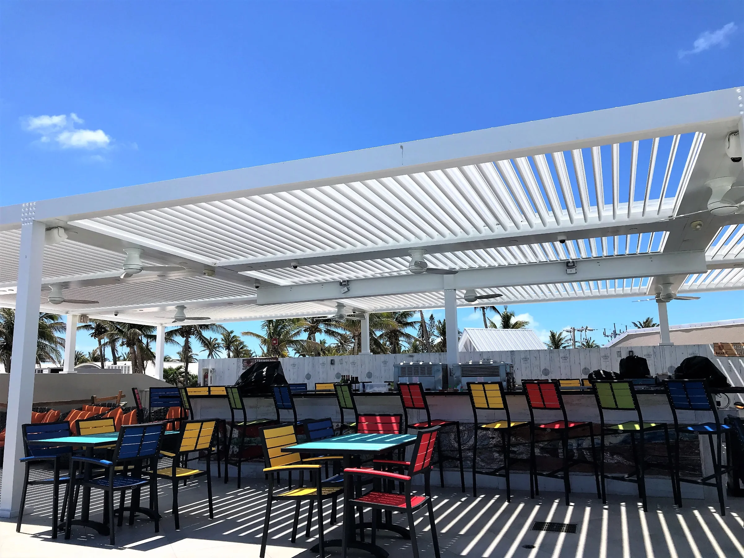 White louvered pergola shading waterfront restaurant seating beside turquoise water