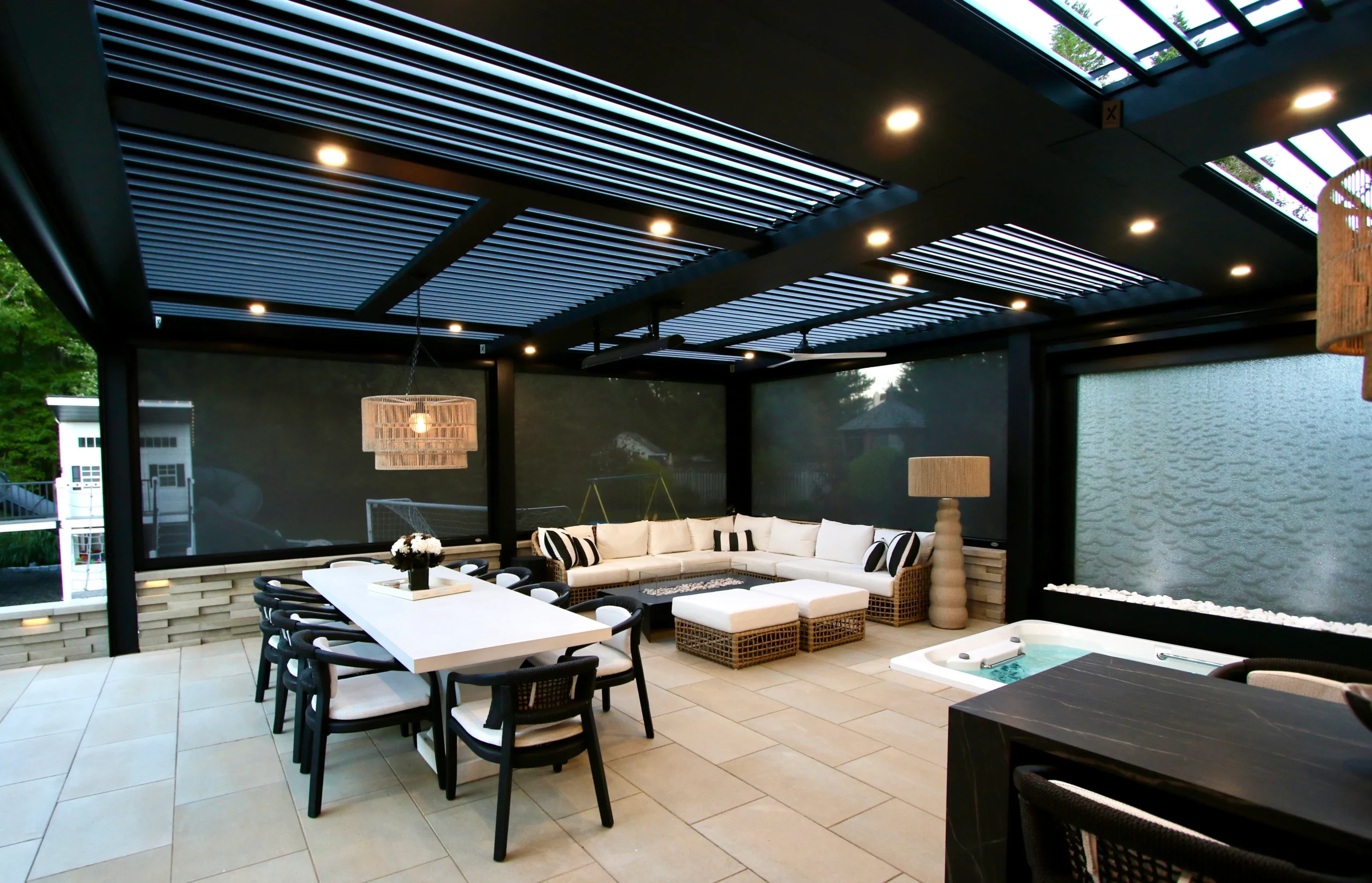 Dark louvered pergola over a new outdoor living room with lighting and water feature in Florida