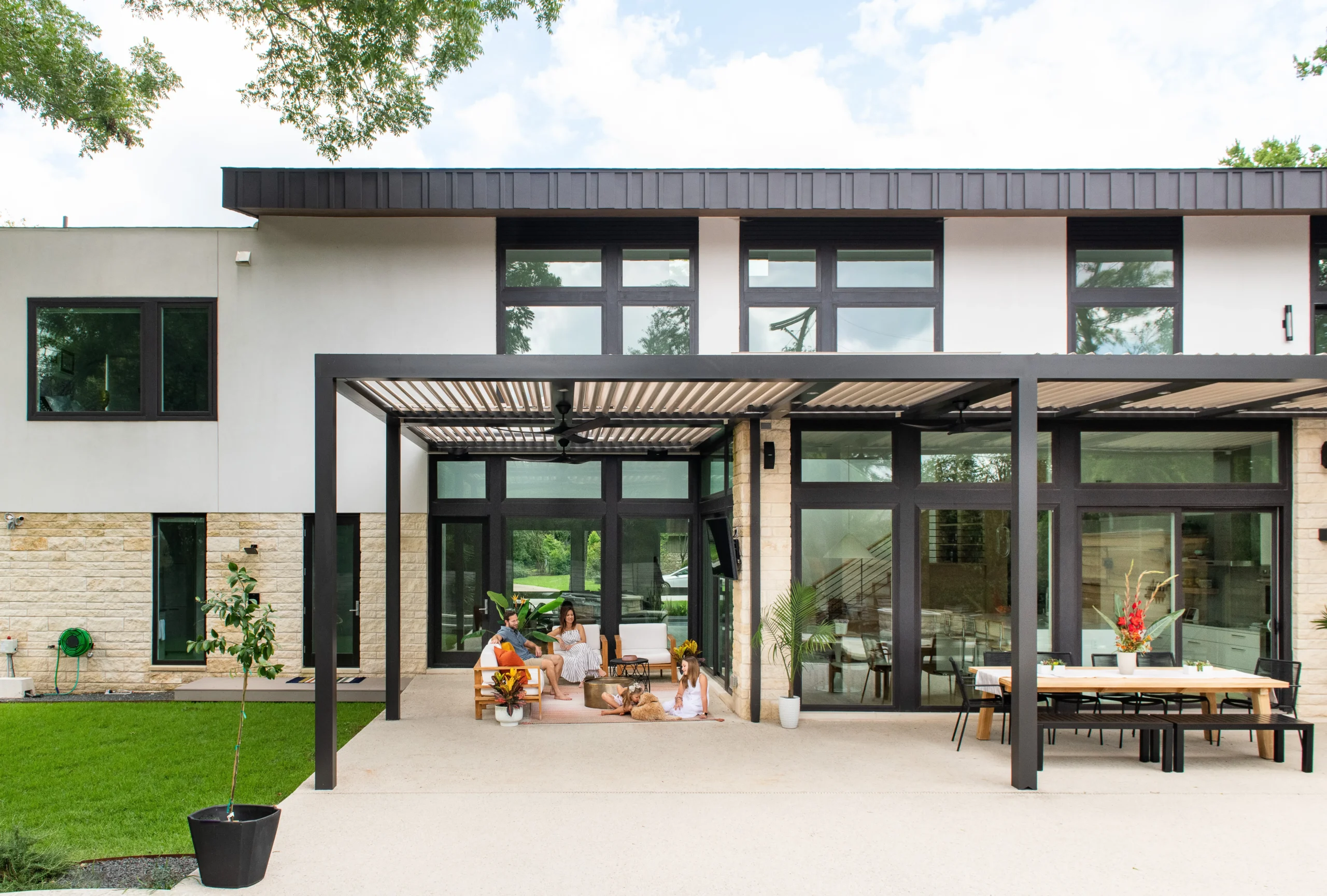 Dark StruXure pergola at a modern glass residence with a family relaxing on the patio
