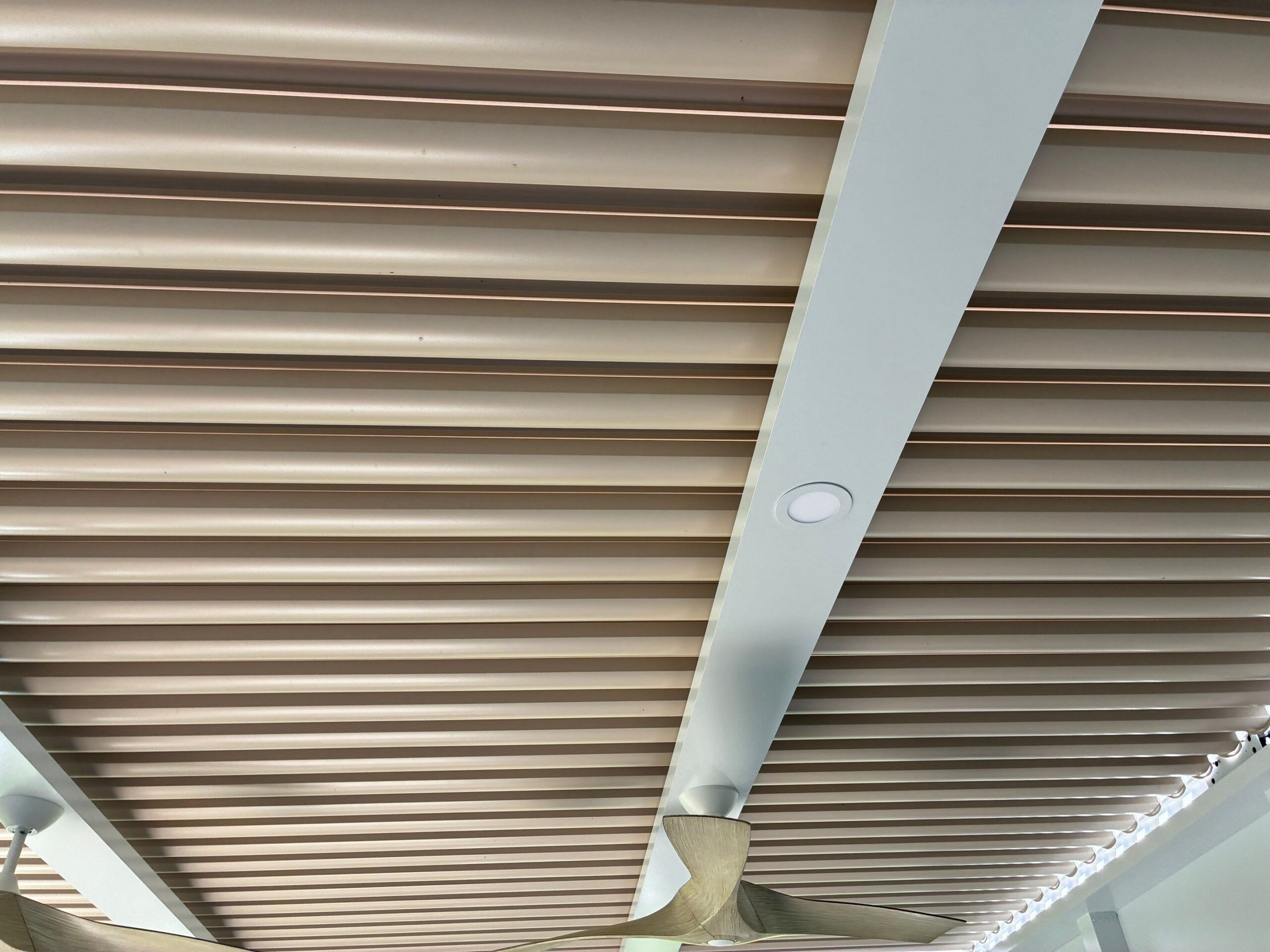 Underside of a tan louvered pergola roof against clear blue sky.