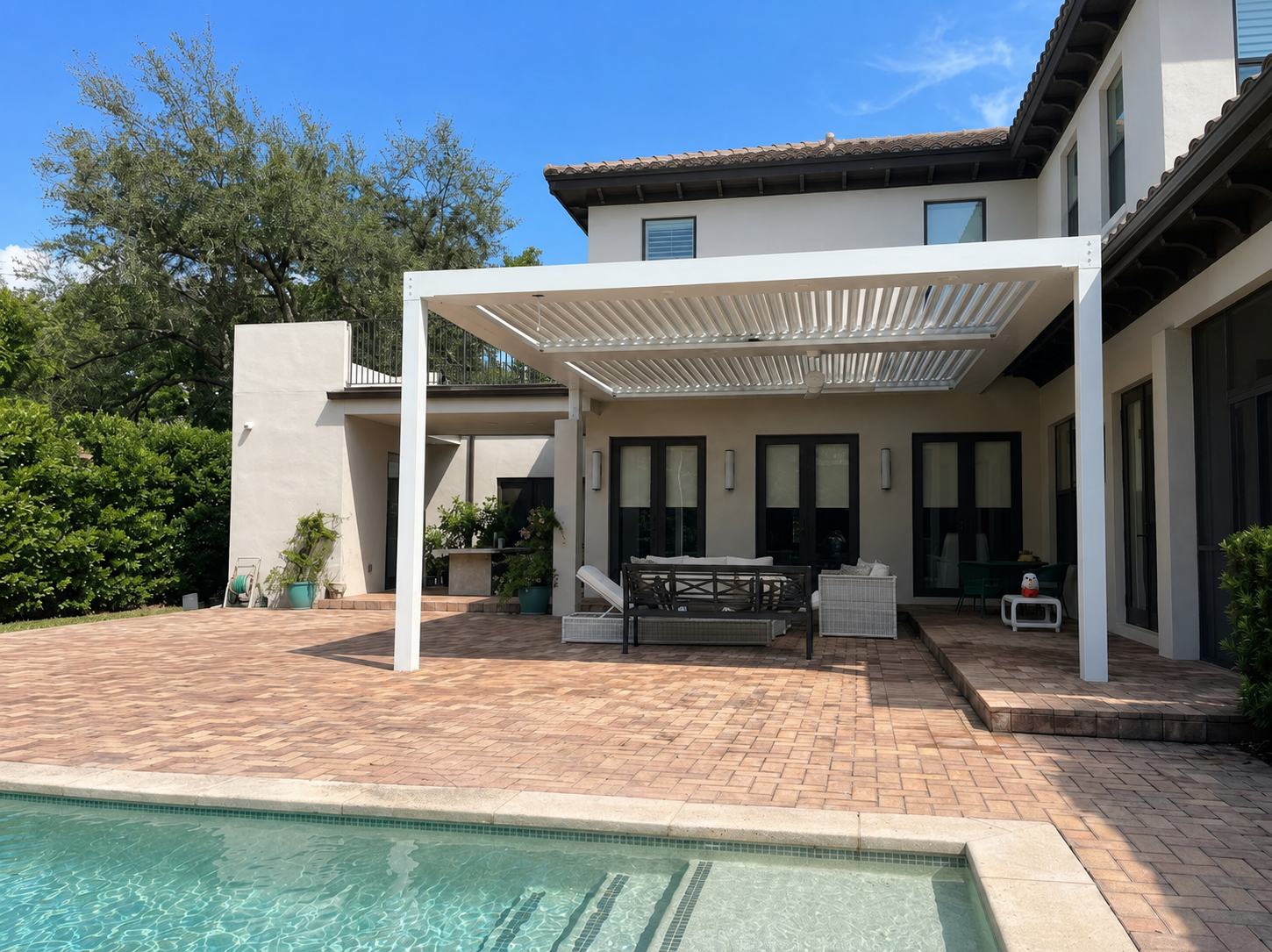 White louvered pergola on a paver patio at a South Florida home with pergola insurance in place