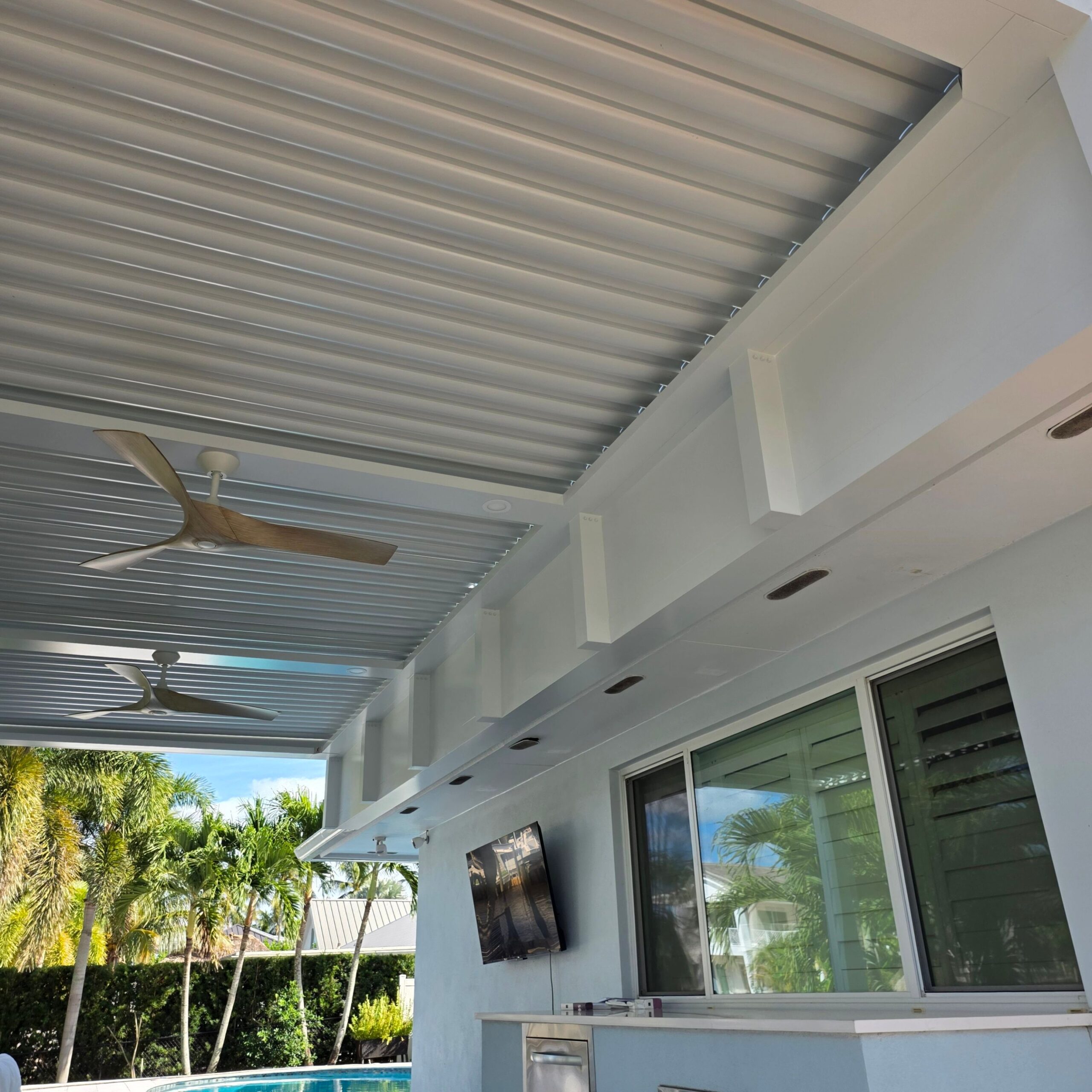 White louvered pergola roof with a ceiling fan above sliding glass doors.