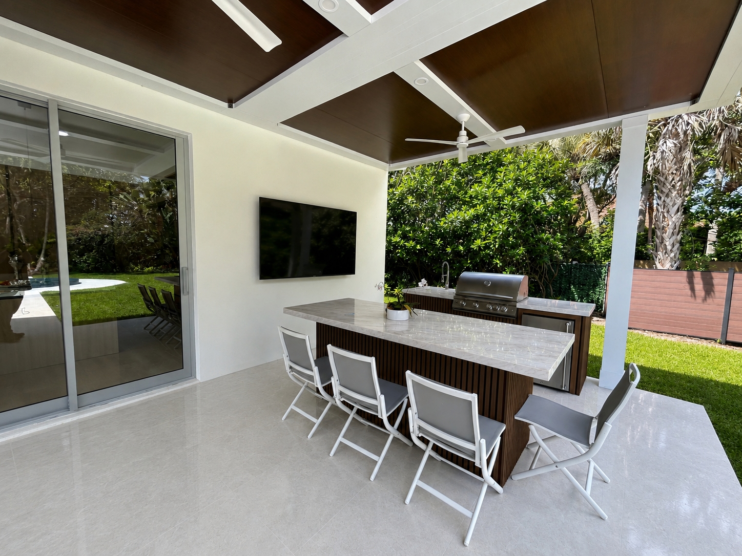 Covered outdoor kitchen with bar seating and a grill under a pergola roof in South Florida